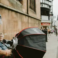 A photographer sets up equipment for a photography fundraiser. A woman in a white and red costume stands in the background.