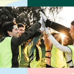A diverse group of young people in bright vests high-five, celebrating their success in volunteer programs for youth.