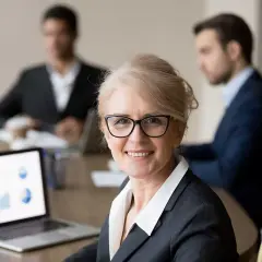 A confident woman leads a board meeting, her laptop displaying charts. This image illustrates how to run a board meeting script effectively.