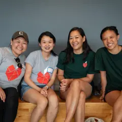 Four smiling women in matching t-shirts with a red heart logo, possibly participating in volunteer opportunities in NYC for college students.