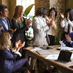 A diverse team applauds, celebrating a successful board fundraising initiative. Their smiles and clapping hands convey a shared sense of accomplishment.