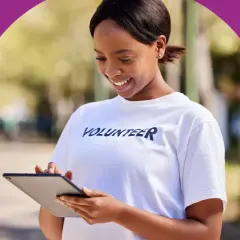 A smiling volunteer in a white t-shirt checks her tablet, perhaps logging hours to show colleges do check volunteer hours.