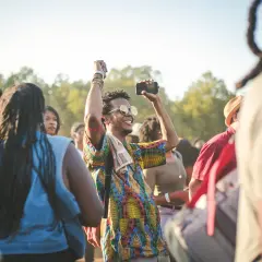 A man with sunglasses and a colorful shirt raises his fist in the air, capturing the energy of a dance-a-thon.