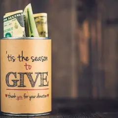 A tin can filled with money, labeled "'tis the season to GIVE," a great example of fundraising sign ideas.