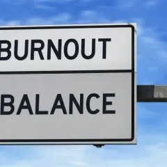 A road sign points to "BURNOUT" straight ahead and "BALANCE" to the right, illustrating the choice between exhaustion and well-being, much like the decision to engage in volunteering.