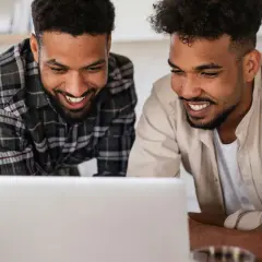 Two men smile at a laptop, possibly reviewing best gofundme examples for their next project.