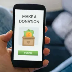 A person uses a donation app on their smartphone, showing a screen with a donation box icon and a "Donate" button.