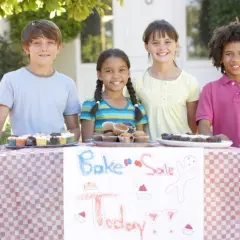 Four kids at a bake sale table, showcasing delicious cupcakes and brownies. Great fundraising ideas for 14 year olds!