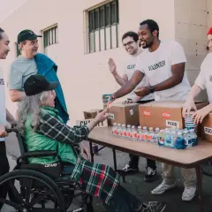 Homeless shelter volunteers hand out water and food to a person in a wheelchair.