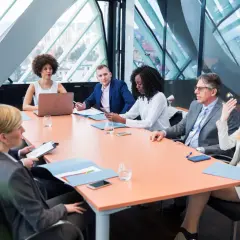 A diverse group of professionals engage in a board meeting, discussing strategy around a large table.