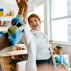 Two women high-five in an office, celebrating a successful project. One holds a coffee cup, perhaps after securing a moz nonprofit discount.