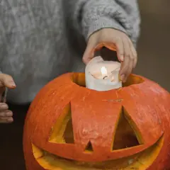 Hands place a lit candle inside a carved pumpkin, a perfect addition to fall festival ideas for work.