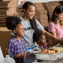 A student volunteer smiles as she helps serve food at a community event.