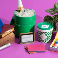 A blue baseball cap with "42" on it, books, a green ice bucket with a bottle, Maldon salt, an e-reader, a passport holder, and a box of chocolates. Small prize ideas for adults.