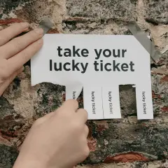 Hands tear off "lucky ticket" strips from a poster on a brick wall, offering great raffle ideas.