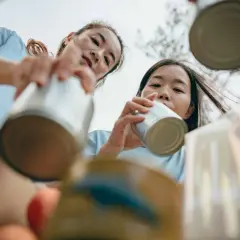 Two young women participate in voluntary community service, sorting cans for recycling.