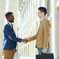 Two businessmen shake hands outside a modern building, perhaps after a successful meeting facilitated by their board portal.