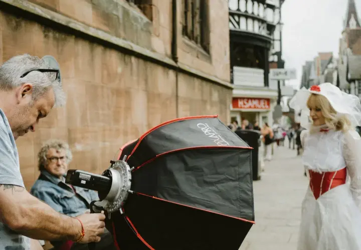 A photographer sets up equipment for a photography fundraiser. A woman in a white and red costume stands in the background.