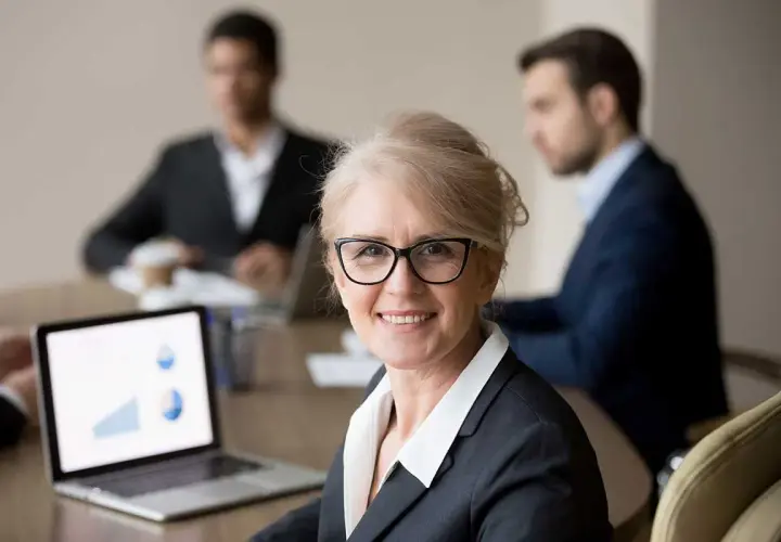 A confident woman leads a board meeting, her laptop displaying charts. This image illustrates how to run a board meeting script effectively.