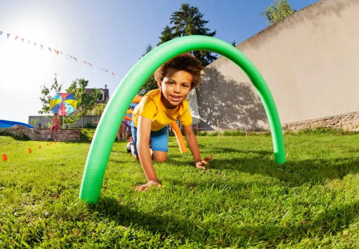 A boy crawls through a green pool noodle arch at a fun elementary school fall festival. Great ideas for outdoor games!