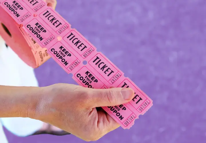 Hands hold a roll of pink raffle tickets, ready to be torn off for big ticket raffle items.