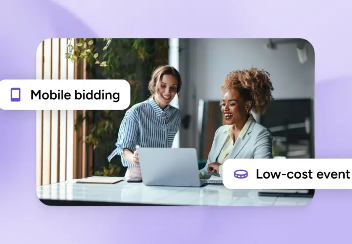 Two women smile while looking at a laptop, suggesting inexpensive silent auction ideas through mobile bidding for a low-cost event.
