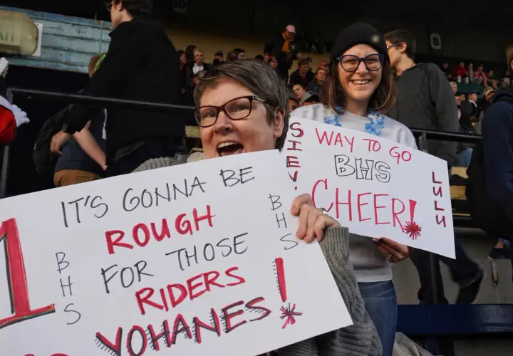 Fans hold signs at a snap raise fundraiser. One sign reads "IT'S GONNA BE ROUGH FOR THOSE RIDERS YOHANES!