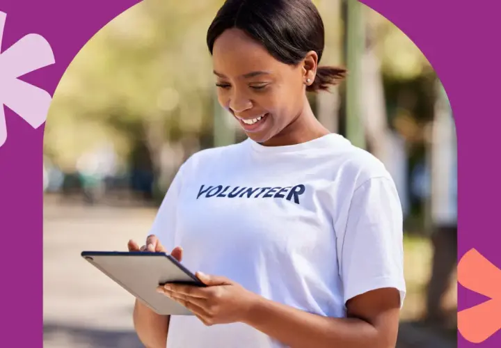 A smiling volunteer in a white t-shirt checks her tablet, perhaps logging hours to show colleges do check volunteer hours.