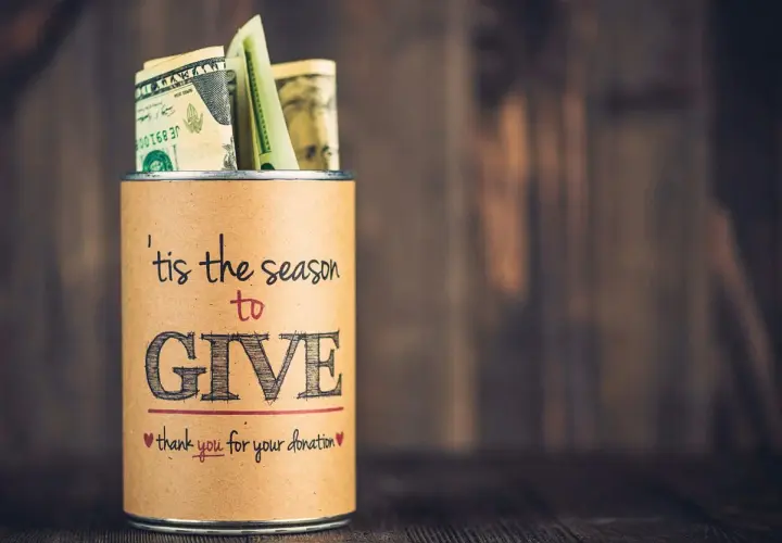 A tin can filled with money, labeled "'tis the season to GIVE," a great example of fundraising sign ideas.