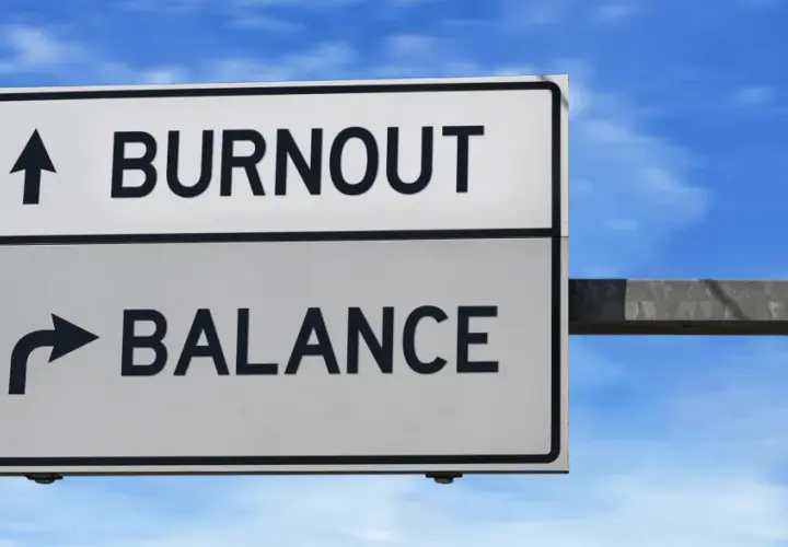 A road sign points to "BURNOUT" straight ahead and "BALANCE" to the right, illustrating the choice between exhaustion and well-being, much like the decision to engage in volunteering.