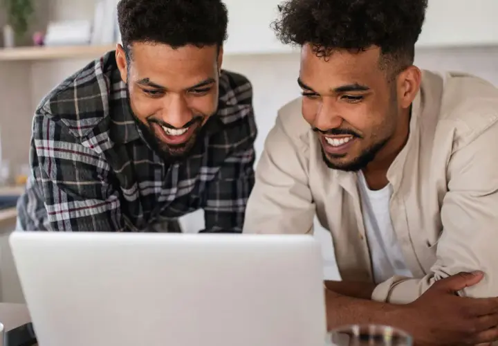 Two men smile at a laptop, possibly reviewing best gofundme examples for their next project.