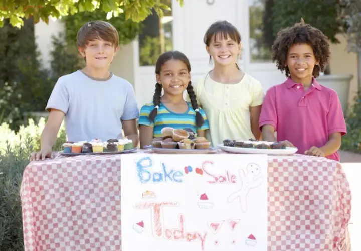 Four kids at a bake sale table, showcasing delicious cupcakes and brownies. Great fundraising ideas for 14 year olds!