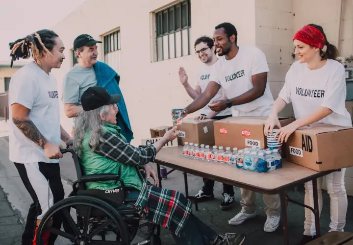 Homeless shelter volunteers hand out water and food to a person in a wheelchair.