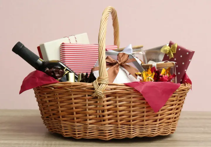 A wicker basket filled with gifts, including a bottle of wine, chocolates, and wrapped presents, perfect for cheap raffle prize ideas.