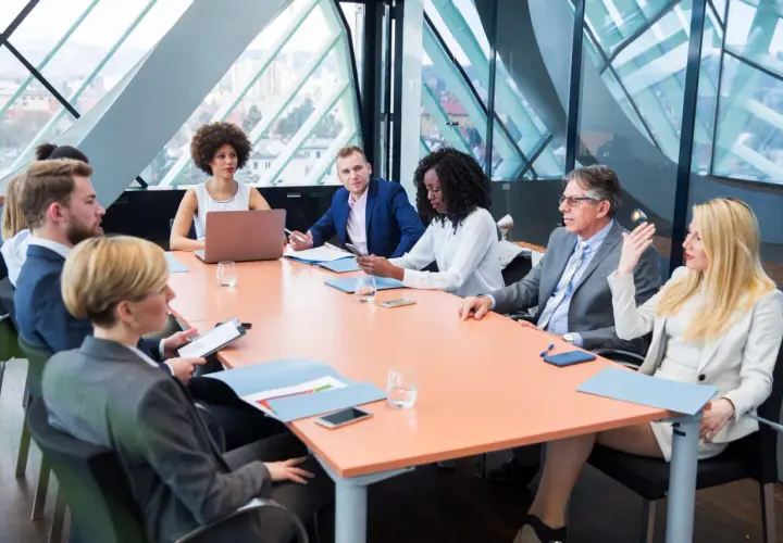 A diverse group of professionals engage in a board meeting, discussing strategy around a large table.