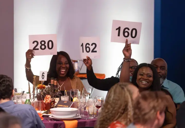 Excited guests participate in a paddle raise fundraiser, holding up signs with numbers like 280, 162, and 160.