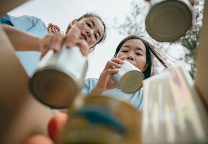 Two young women participate in DEI volunteer opportunities, sorting cans for recycling.