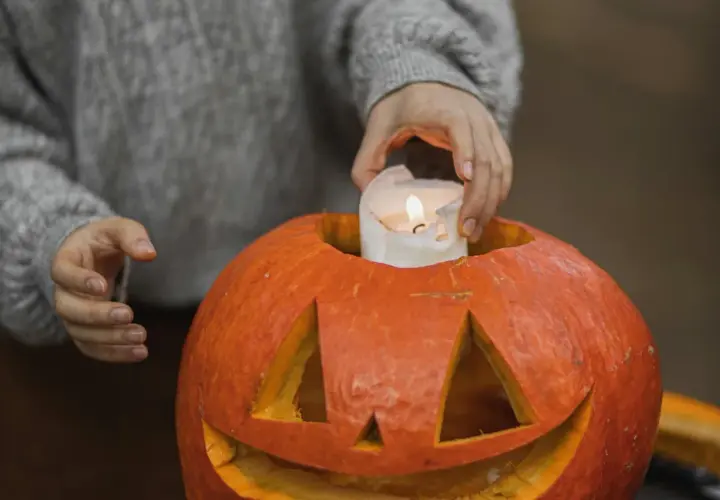 Hands place a lit candle inside a carved pumpkin, a perfect addition to fall festival ideas for work.