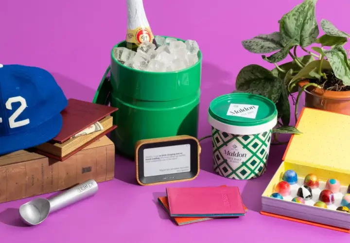 A blue baseball cap with "42" on it, books, a green ice bucket with a bottle, Maldon salt, an e-reader, a passport holder, and a box of chocolates. Small prize ideas for adults.