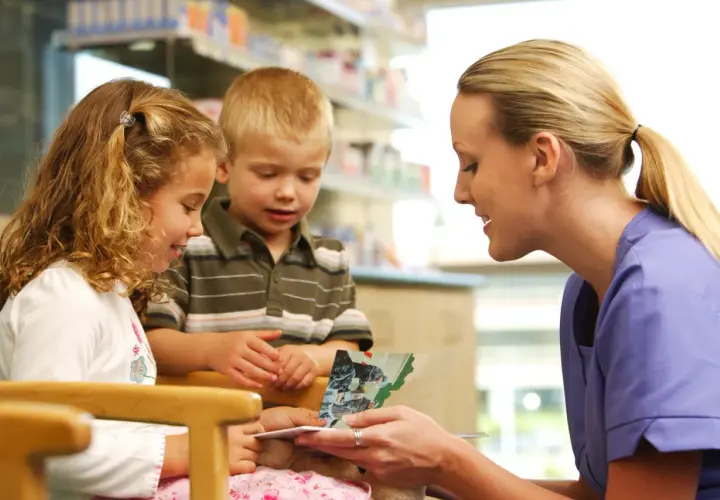A Kaiser Permanente volunteer program member reads a book to two children in a bright, clean setting.