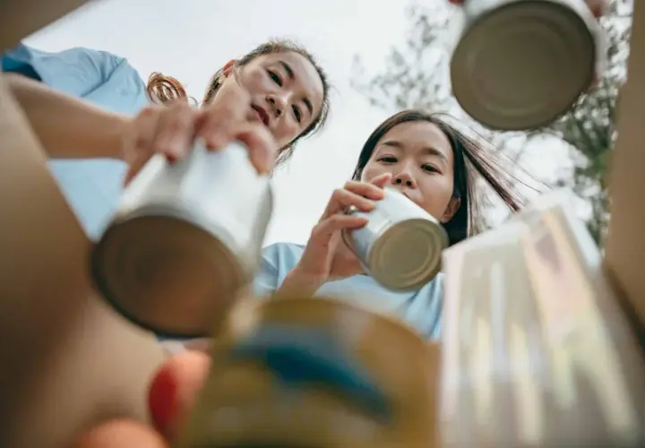 Two young women participate in voluntary community service, sorting cans for recycling.