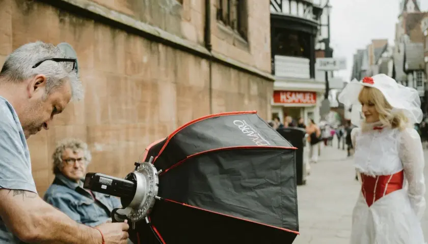 A photographer sets up equipment for a photography fundraiser. A woman in a white and red costume stands in the background.