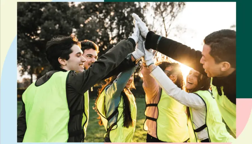 A diverse group of young people in bright vests high-five, celebrating their success in volunteer programs for youth.