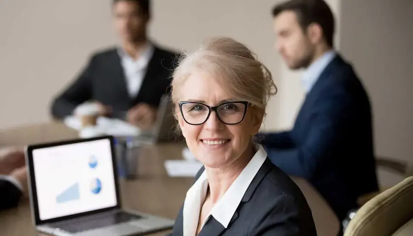 A confident woman leads a board meeting, her laptop displaying charts. This image illustrates how to run a board meeting script effectively.