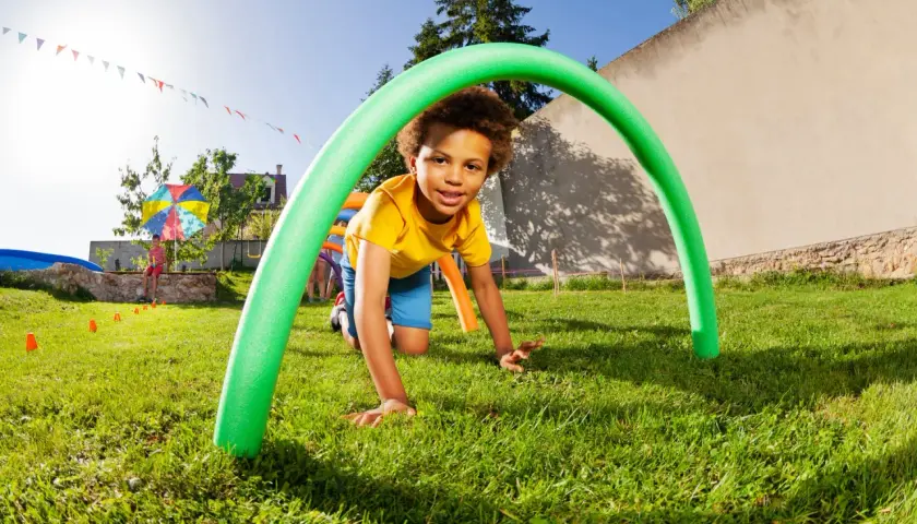 A boy crawls through a green pool noodle arch at a fun elementary school fall festival. Great ideas for outdoor games!
