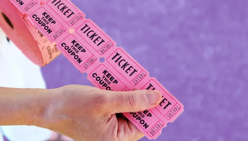 Hands hold a roll of pink raffle tickets, ready to be torn off for big ticket raffle items.