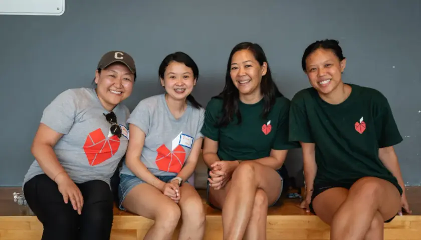 Four smiling women in matching t-shirts with a red heart logo, possibly participating in volunteer opportunities in NYC for college students.