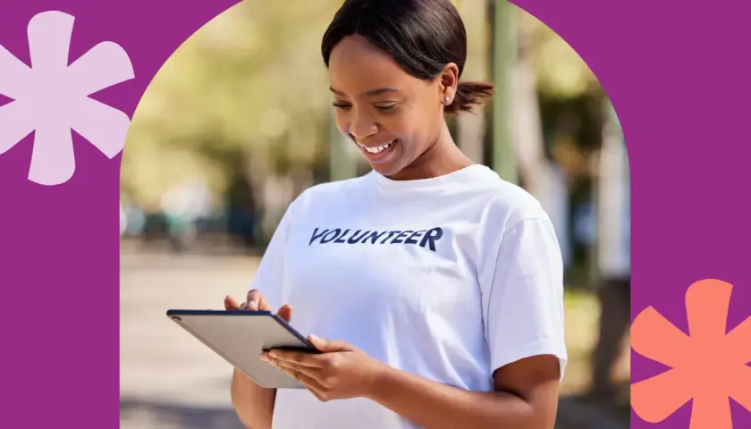 A smiling volunteer in a white t-shirt checks her tablet, perhaps logging hours to show colleges do check volunteer hours.