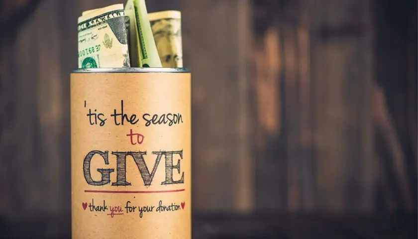 A tin can filled with money, labeled "'tis the season to GIVE," a great example of fundraising sign ideas.