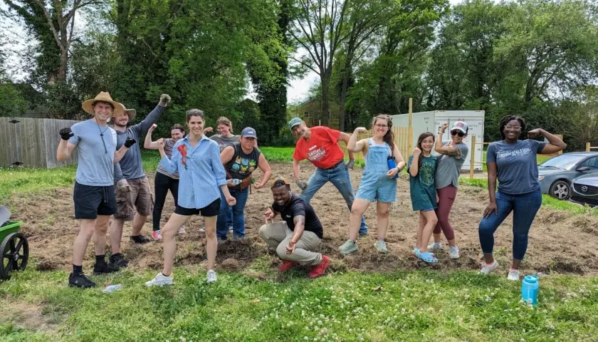 A diverse group of volunteers flexes their muscles, celebrating their hard work on a community service project.